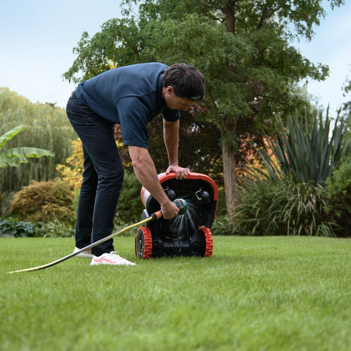 Man cleans the Navimow i105E robot lawn mower with water.