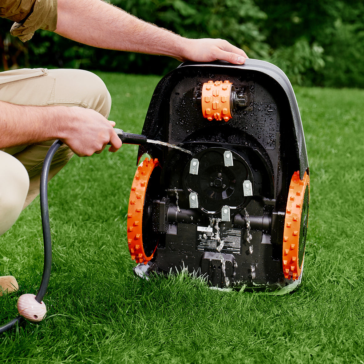 Navimow i105E robot lawn mower being washed with garden hose.